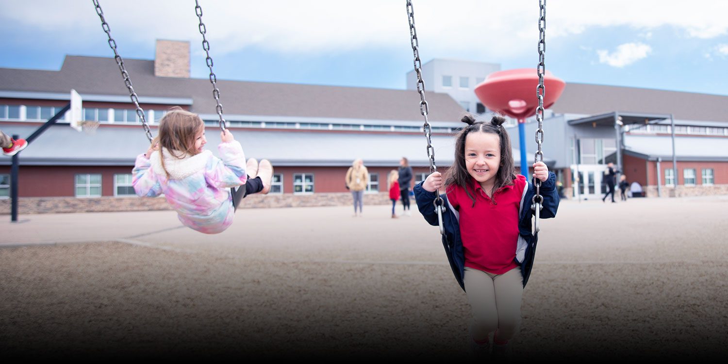 students on swings smiling at the playing ground.